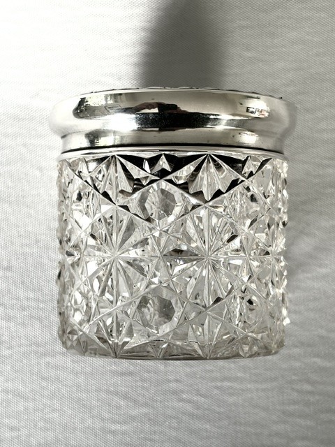 A round cut glass vanity jar topped with a hallmarked sterling silver lid featuring a central blue floral enamel motif. View X