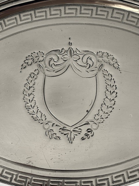 An oval Georgian silver teapot stand featuring an engraved Greek key border, a central cartouche, and four small supportive feet. View VI