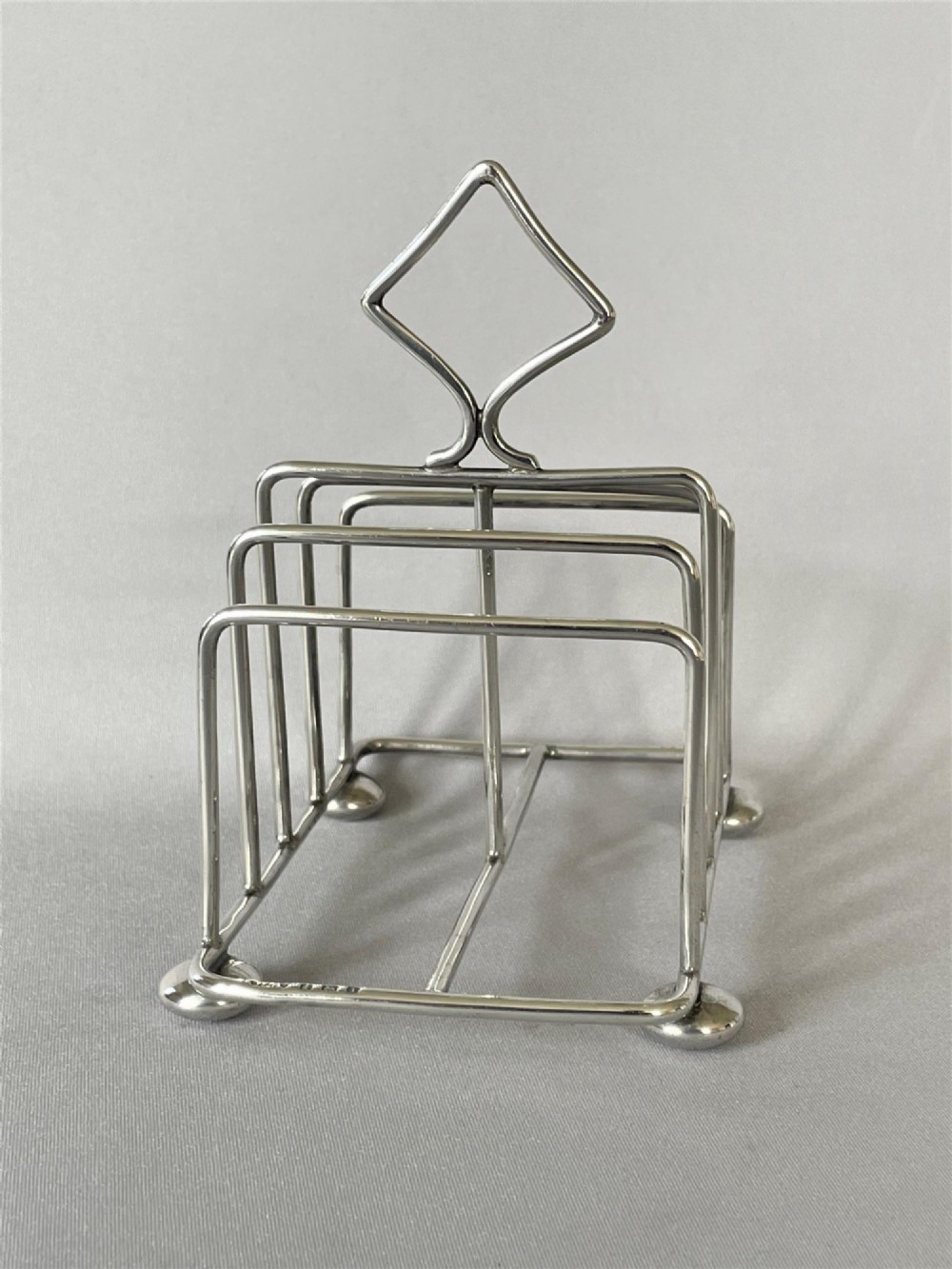 An Edwardian silver toast rack featuring four divisions, four ball feet, and a central diamond-shaped loop handle. View III