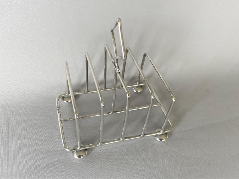 An Edwardian silver toast rack featuring four divisions, four ball feet, and a central diamond-shaped loop handle. View VI