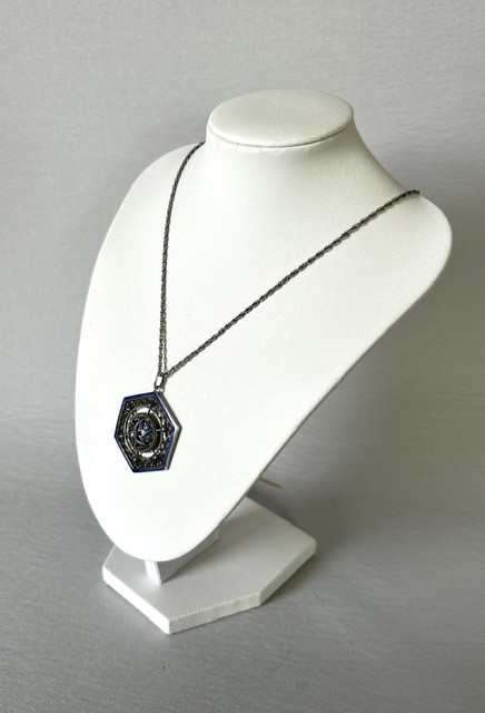 A hexagonal silver pendant with delicate wire filigree scrolls surrounding a central blue guilloche enamel dome, suspended from a silver chain. View VII