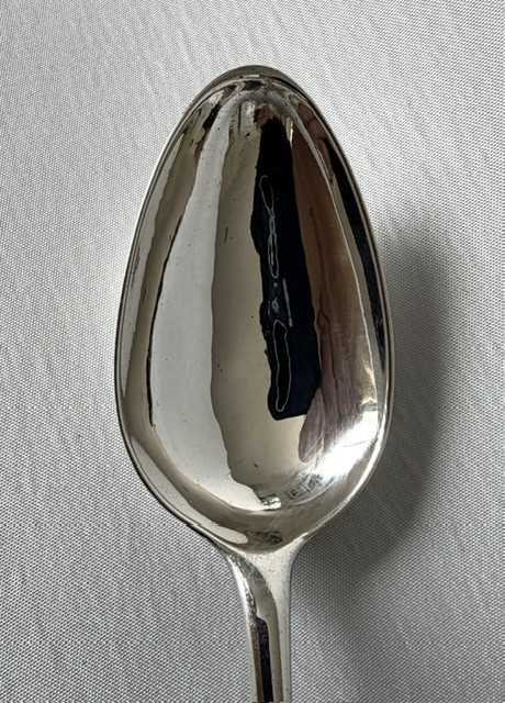 An 18th-century sterling silver serving spoon featuring an oval bowl and a tapered stem stamped with provincial hallmarks near the terminal. View IV