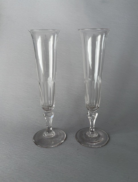 A pair of clear early Victorian cut glass champagne flutes featuring flared rims, faceted stems, and slice-cut lower bowls on flat circular bases.