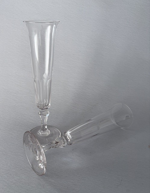 A pair of clear early Victorian cut glass champagne flutes featuring flared rims, faceted stems, and slice-cut lower bowls on flat circular bases. View V