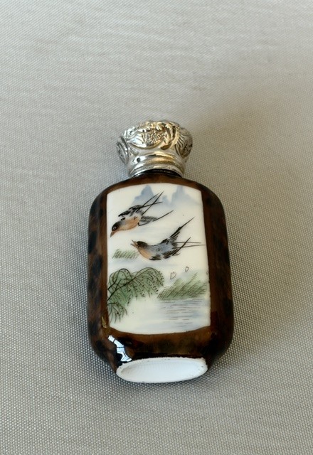 A small flattened oval scent bottle featuring a mottled brown body, a white enamel panel with a hand-painted bird among reeds, and a embossed silver cap. View III