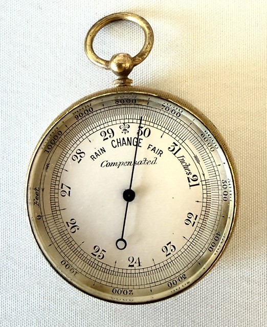 An Edwardian brass pocket barometer and altimeter displayed inside an open plush-lined maroon leather case. View IV