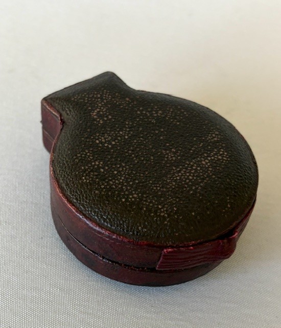 An Edwardian brass pocket barometer and altimeter displayed inside an open plush-lined maroon leather case. View VII