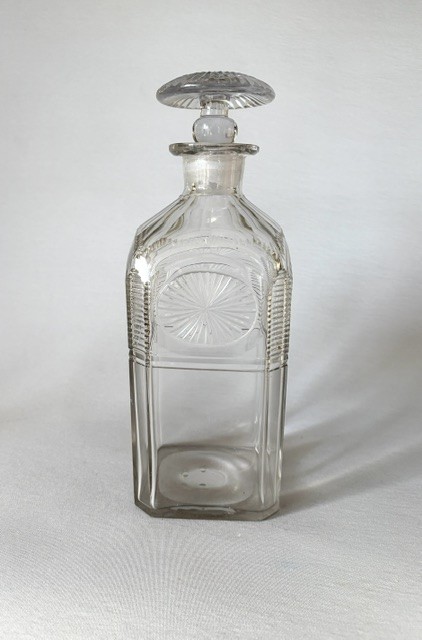 A square clear cut glass decanter featuring wheel-cut starburst motifs, faceted shoulders, and a flat mushroom stopper. View II