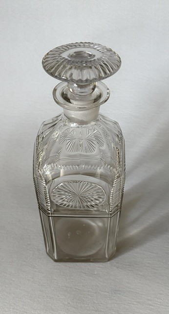 A square clear cut glass decanter featuring wheel-cut starburst motifs, faceted shoulders, and a flat mushroom stopper. View III