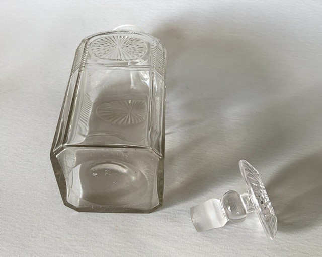 A square clear cut glass decanter featuring wheel-cut starburst motifs, faceted shoulders, and a flat mushroom stopper. View VI