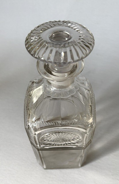 A square clear cut glass decanter featuring wheel-cut starburst motifs, faceted shoulders, and a flat mushroom stopper. View VII