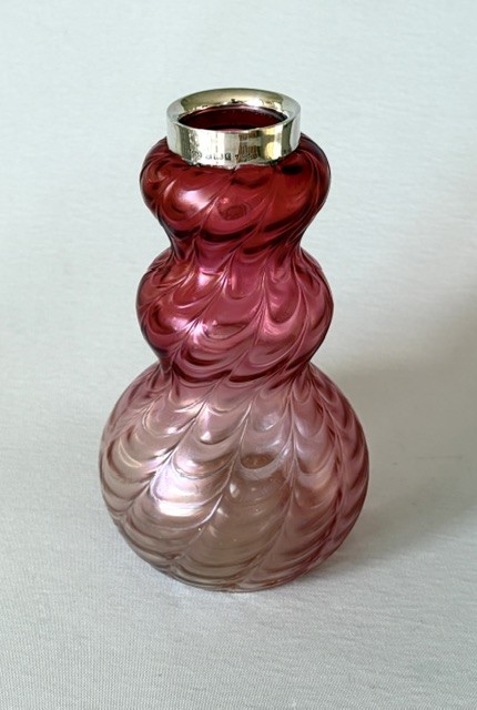 An Art Nouveau iridescent glass vase featuring a lobed, swirling magenta to pink body fitted with a polished sterling silver rim collar.