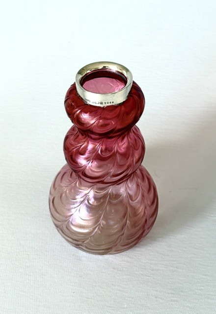 An Art Nouveau iridescent glass vase featuring a lobed, swirling magenta to pink body fitted with a polished sterling silver rim collar. View II