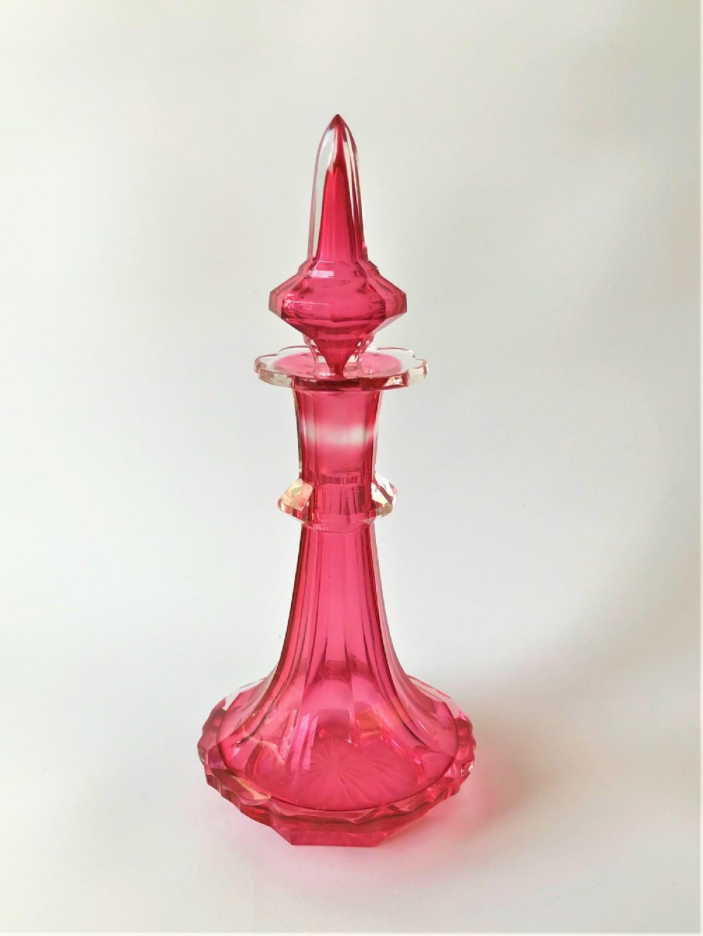A tall Victorian cranberry and clear cut glass cologne bottle featuring an elongated pointed spire stopper, faceted neck, and flared base.