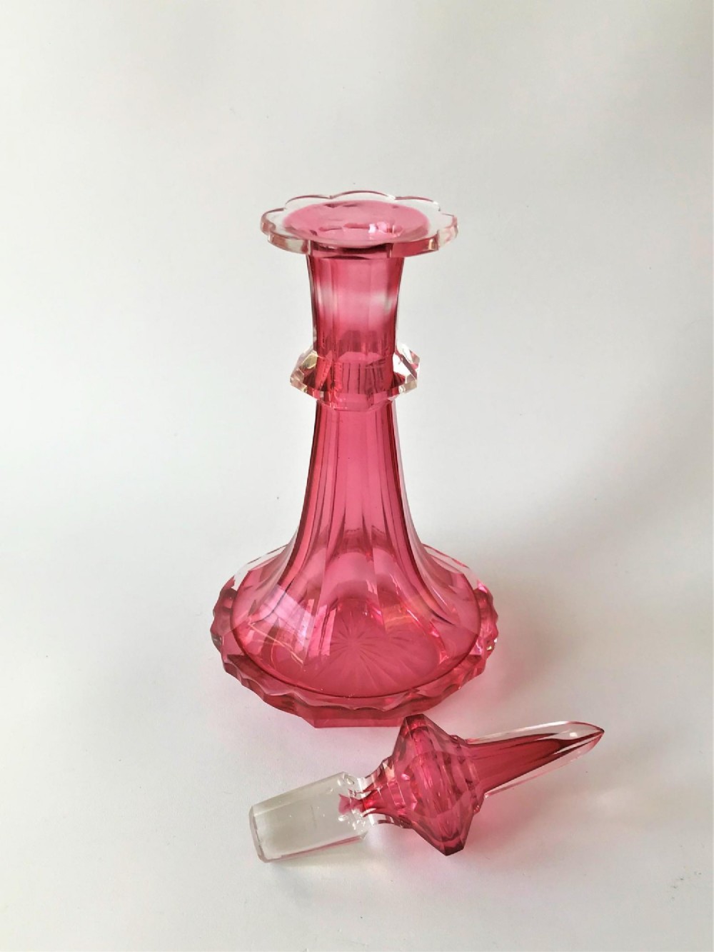 A tall Victorian cranberry and clear cut glass cologne bottle featuring an elongated pointed spire stopper, faceted neck, and flared base. View II