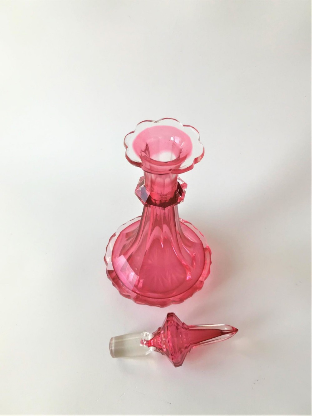 A tall Victorian cranberry and clear cut glass cologne bottle featuring an elongated pointed spire stopper, faceted neck, and flared base. View III