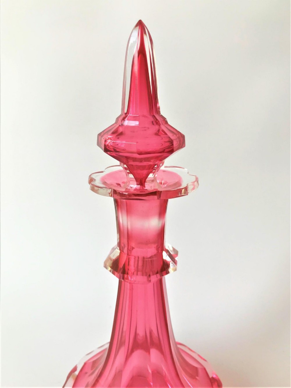 A tall Victorian cranberry and clear cut glass cologne bottle featuring an elongated pointed spire stopper, faceted neck, and flared base. View V