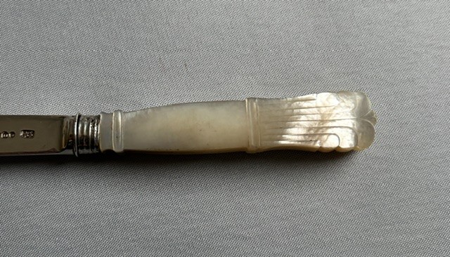 An antique Georgian letter opener featuring a tapered silver blade with stamped hallmarks and a carved cream mother of pearl handle. View VII