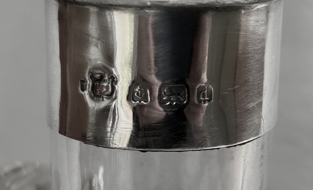 An Edwardian clear glass decanter featuring a bulbous body, three loop handles, a hallmarked sterling silver collar, and a circular glass stopper. View IV