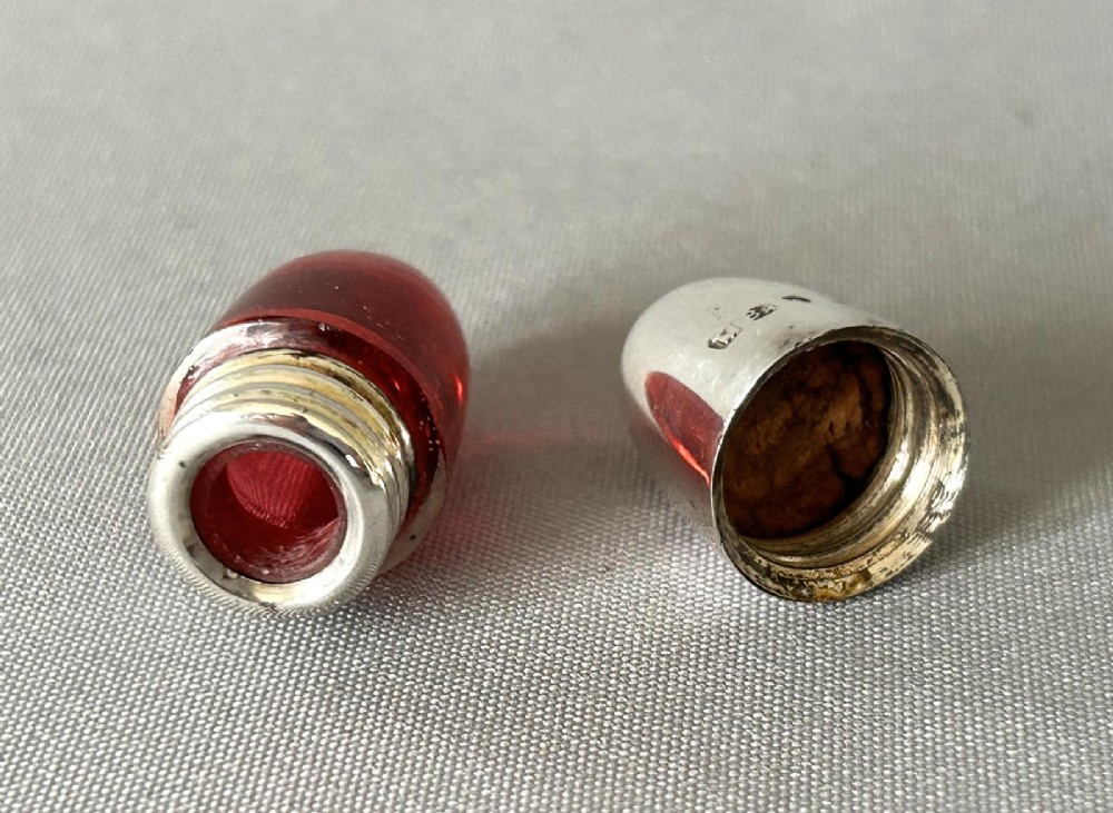 A small bullet-shaped antique scent bottle featuring a polished silver cap and a red cranberry glass body. View V