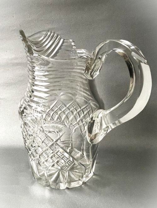A clear cut-glass water jug featuring a loop handle, horizontal step cuts around the neck, and diamond facets across the lower body. View II