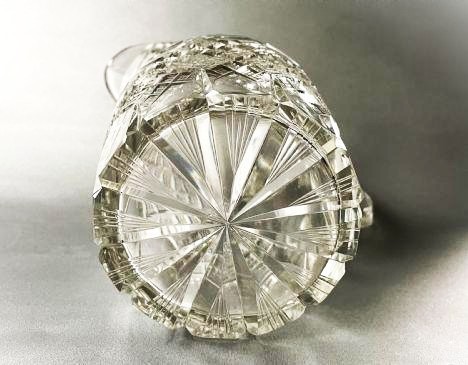A clear cut-glass water jug featuring a loop handle, horizontal step cuts around the neck, and diamond facets across the lower body. View V