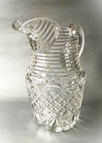 A clear cut-glass water jug featuring a loop handle, horizontal step cuts around the neck, and diamond facets across the lower body. View VI
