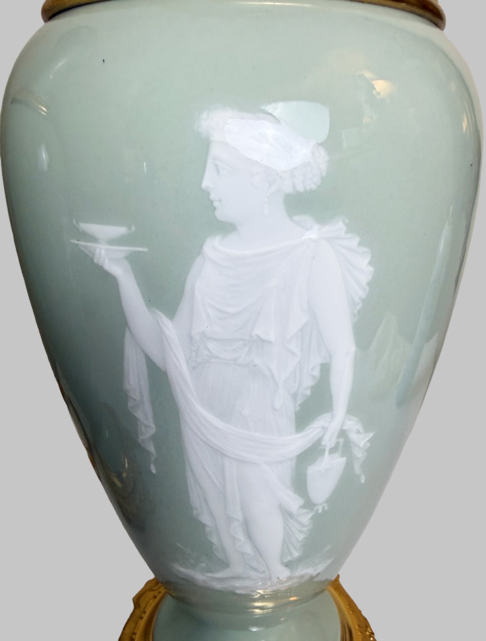 A pair of urn-shaped celadon green porcelain table lamps decorated with white classical figures in low relief, set upon ornate gilded bronze bases. View V