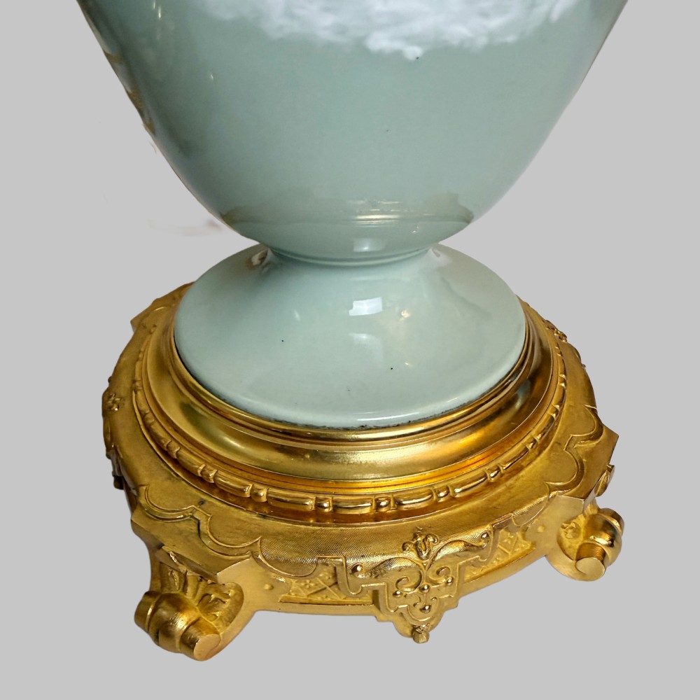 A pair of urn-shaped celadon green porcelain table lamps decorated with white classical figures in low relief, set upon ornate gilded bronze bases. View VI