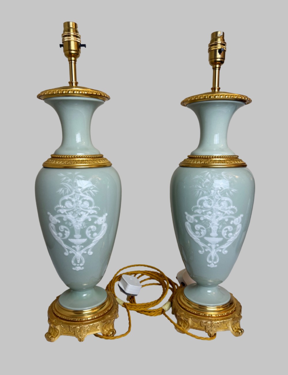 A pair of urn-shaped celadon green porcelain table lamps decorated with white classical figures in low relief, set upon ornate gilded bronze bases. View IX