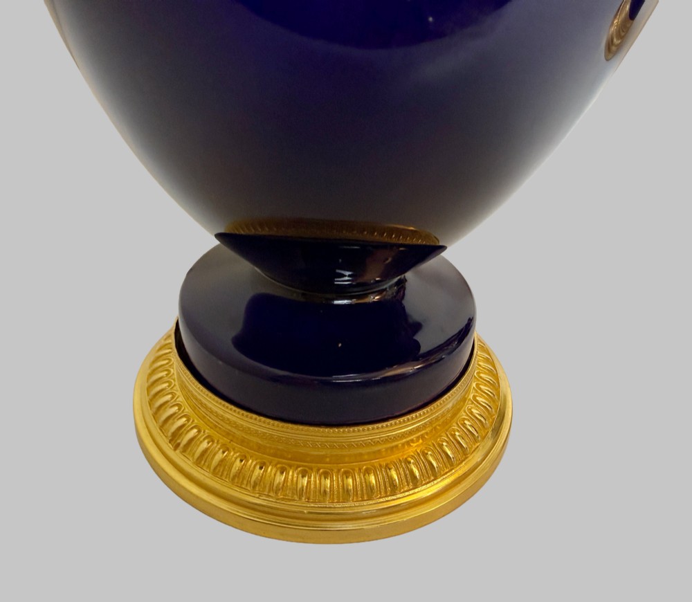 A pair of slender 19th-century cobalt blue porcelain vases featuring gilt bronze beaded rims, floral garland mounts, and circular cast pedestals. View V