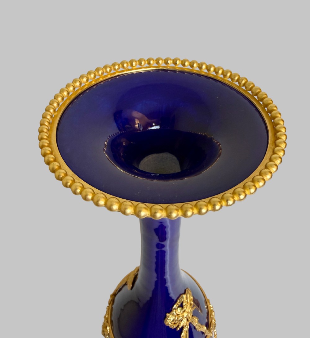 A pair of slender 19th-century cobalt blue porcelain vases featuring gilt bronze beaded rims, floral garland mounts, and circular cast pedestals. View VII