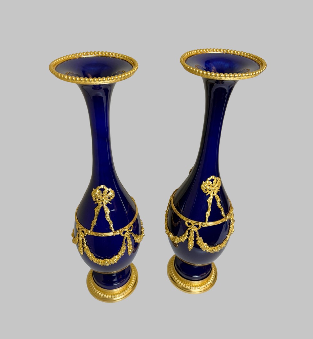 A pair of slender 19th-century cobalt blue porcelain vases featuring gilt bronze beaded rims, floral garland mounts, and circular cast pedestals. View VIII