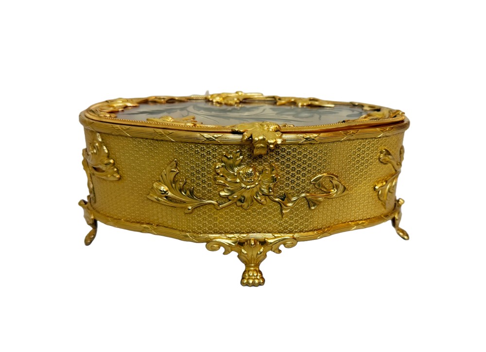 An oval nineteenth-century gilt bronze jewellery box featuring textured foliate relief work, scroll feet, and an etched glass lid.