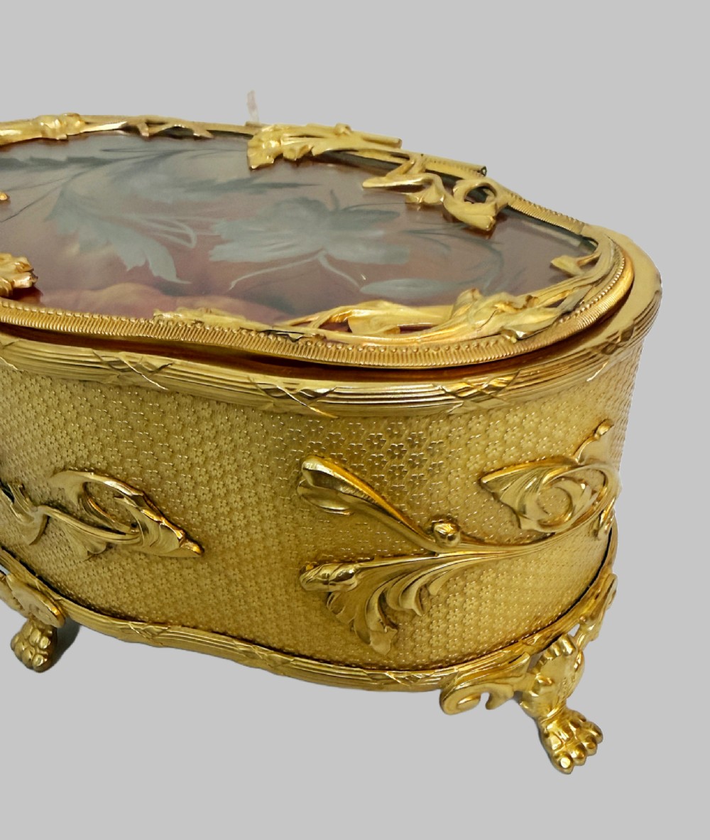 An oval nineteenth-century gilt bronze jewellery box featuring textured foliate relief work, scroll feet, and an etched glass lid. View IV
