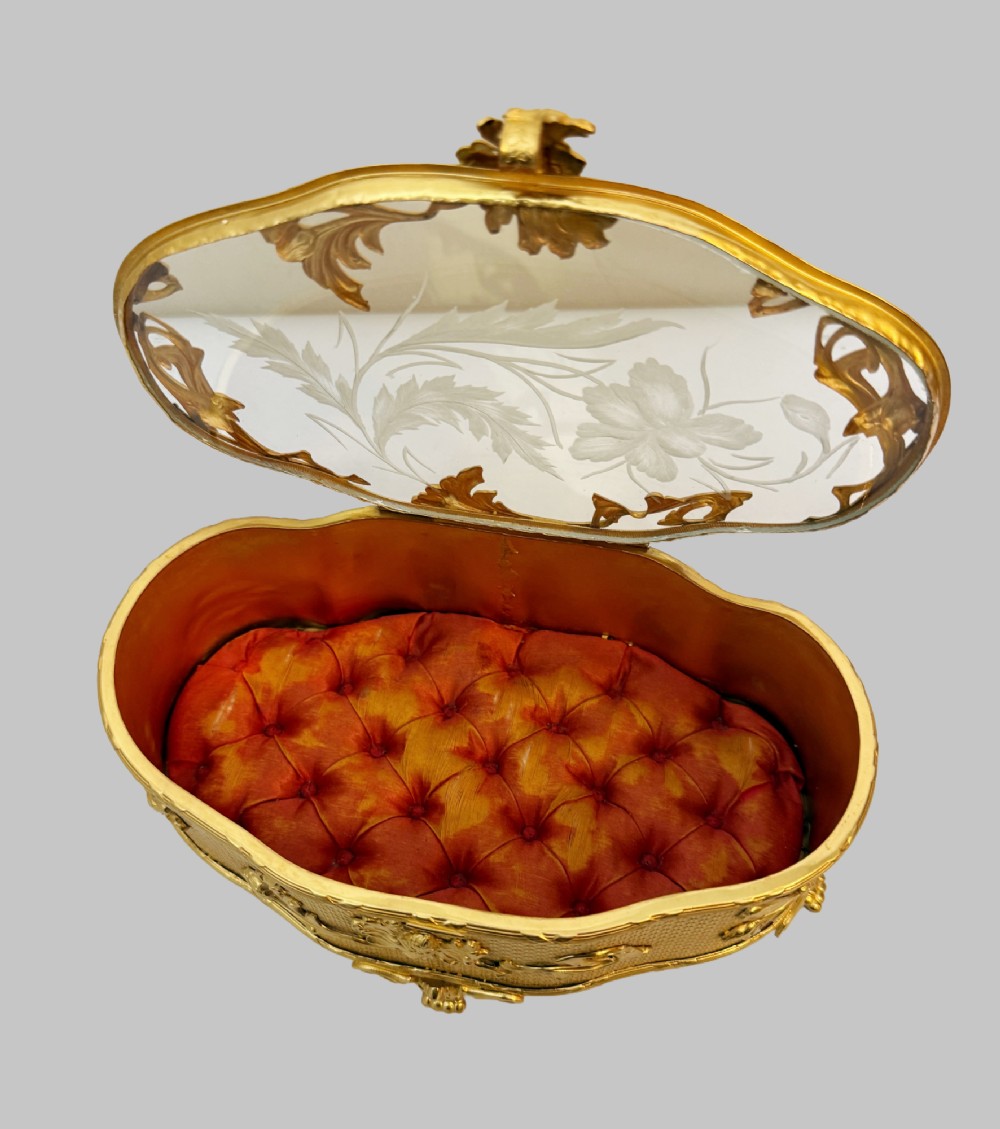 An oval nineteenth-century gilt bronze jewellery box featuring textured foliate relief work, scroll feet, and an etched glass lid. View V