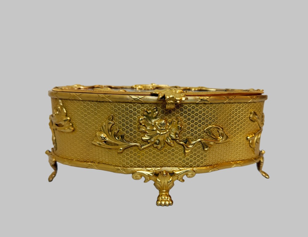 An oval nineteenth-century gilt bronze jewellery box featuring textured foliate relief work, scroll feet, and an etched glass lid. View IX