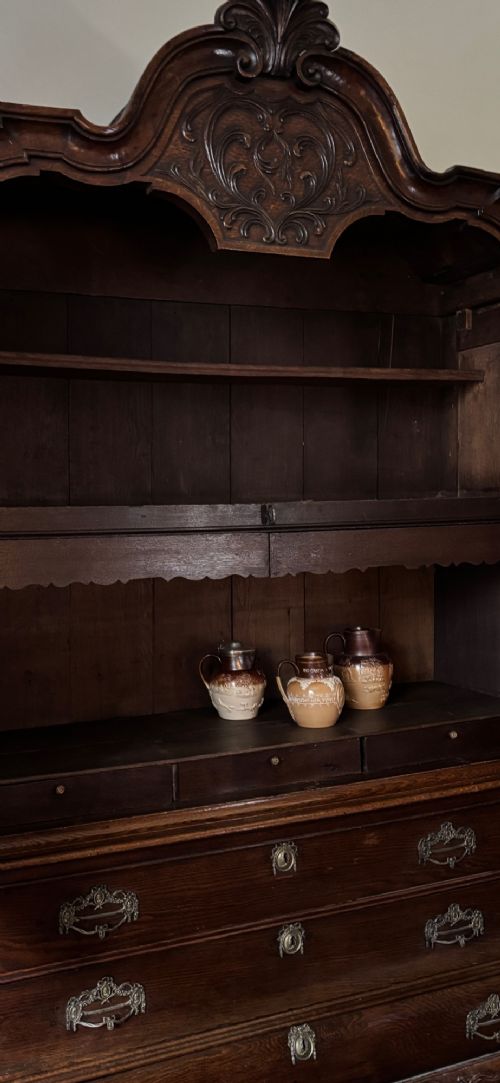 An 18th-century Dutch carved oak linen press featuring contoured panel doors, a carved cresting pediment, brass handles, and a bombee lower section with drawers. View VIII