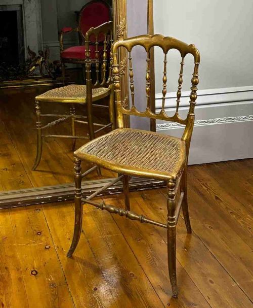 A 19th-century French giltwood salon chair featuring turned spindles, a woven cane seat, and slender curved legs with a distressed gold finish.