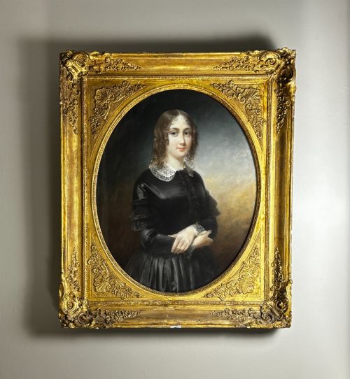 fig 1. A Victorian portrait painting depicting a seated woman with ringlets in a dark dress with a lace collar, framed within an ornate gold gilded frame with an oval aperture.