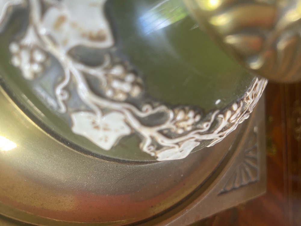 An Edwardian table lamp featuring a stepped square brass base, a dark cylindrical ceramic column decorated with white relief foliage, and a cream pleated shade with tassel fringe. View IV
