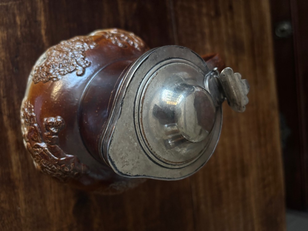 An 18th-century Mortlake salt-glazed stoneware ale pitcher with raised tavern sprigged reliefs and a silver-plated hinged lid. View VII