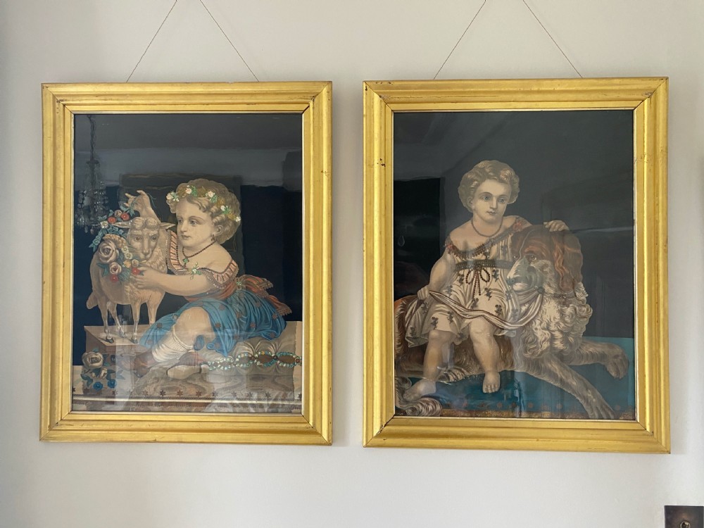 A pair of framed nineteenth-century portrait prints depicting children with animals, featuring metallic foil embellishments on their attire, housed in moulded giltwood frames.