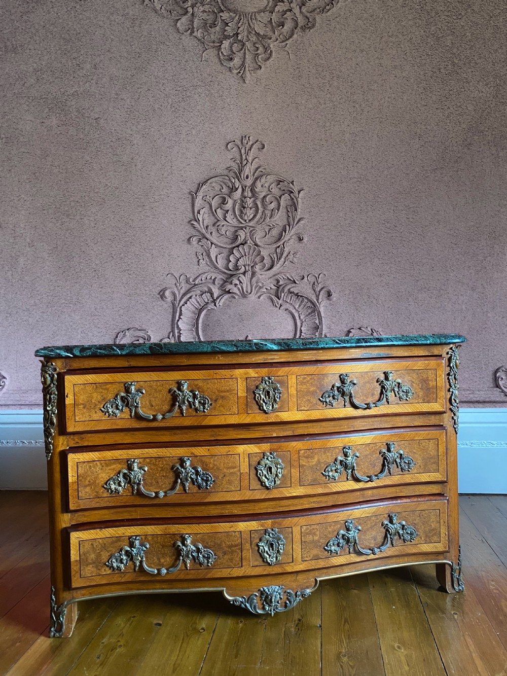 A three-drawer Louis XV style wooden commode featuring a green marble top, serpentine front, timber veneering, and ornate gilt metal mounts. View II