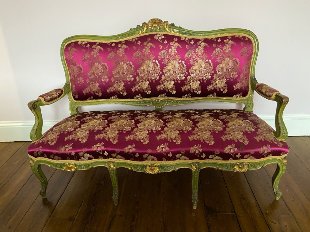 An early 19th-century Italian Venetian sofa featuring a carved green and gold polychrome frame with cabriole legs, upholstered in a rich magenta floral damask fabric.