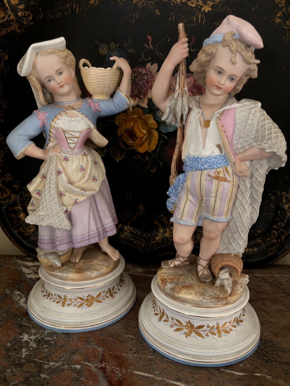 A pair of antique French hand-painted porcelain figurines depicting a young man and woman dressed in traditional fisher folk attire, standing on gilded circular bases.