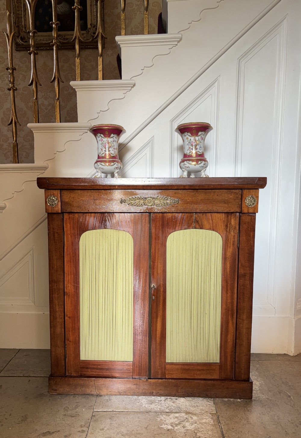 A late Regency rosewood side cabinet featuring two doors with arched pleated fabric panels and central brass decorative mounts. View II