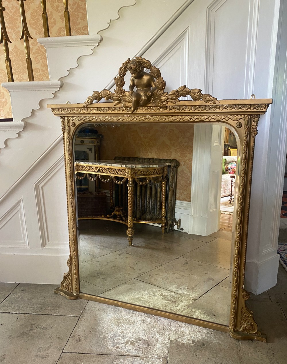A late 19th-century giltwood overmantel mirror featuring an arched inner frame topped with a sculpted cherub and laurel leaf pediment.