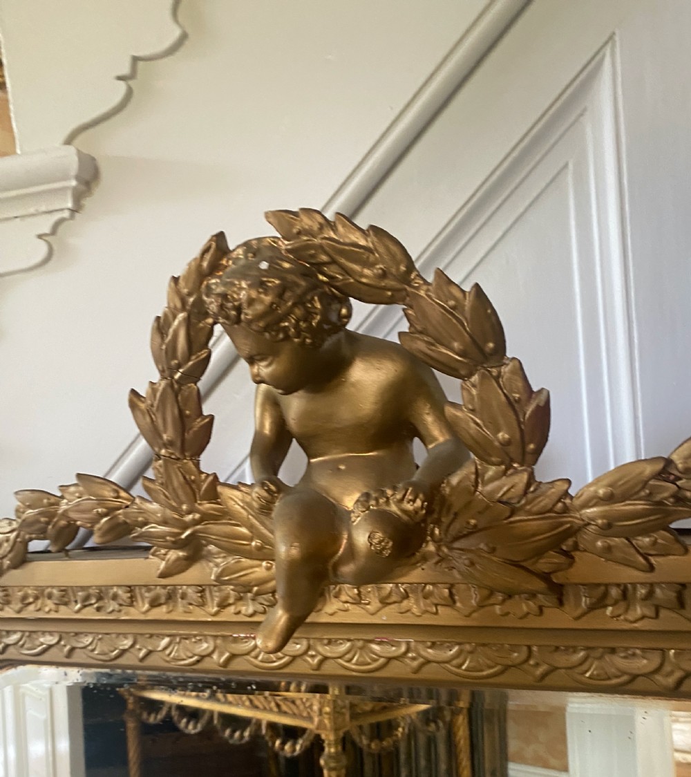 A late 19th-century giltwood overmantel mirror featuring an arched inner frame topped with a sculpted cherub and laurel leaf pediment. View III