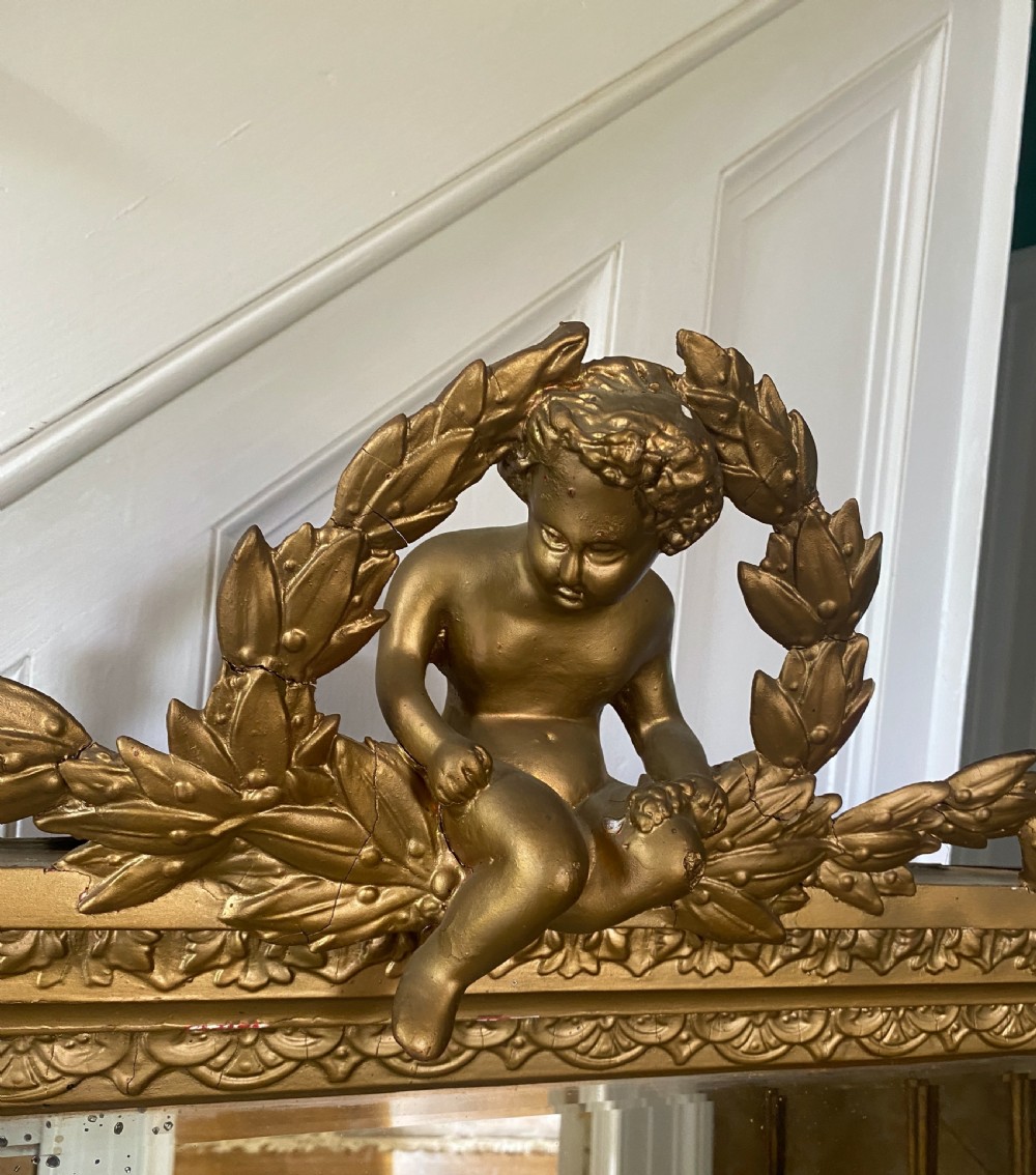 A late 19th-century giltwood overmantel mirror featuring an arched inner frame topped with a sculpted cherub and laurel leaf pediment. View IV